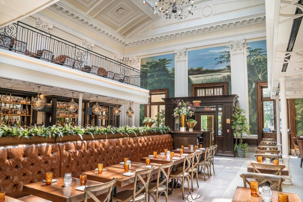 light and bright interior of Succotash with high ceilings, gorgeous chandeliers, a stunning multi-paneled, full wall, nature mural, and a 2nd level overlooking the bar and luxurious booths below
