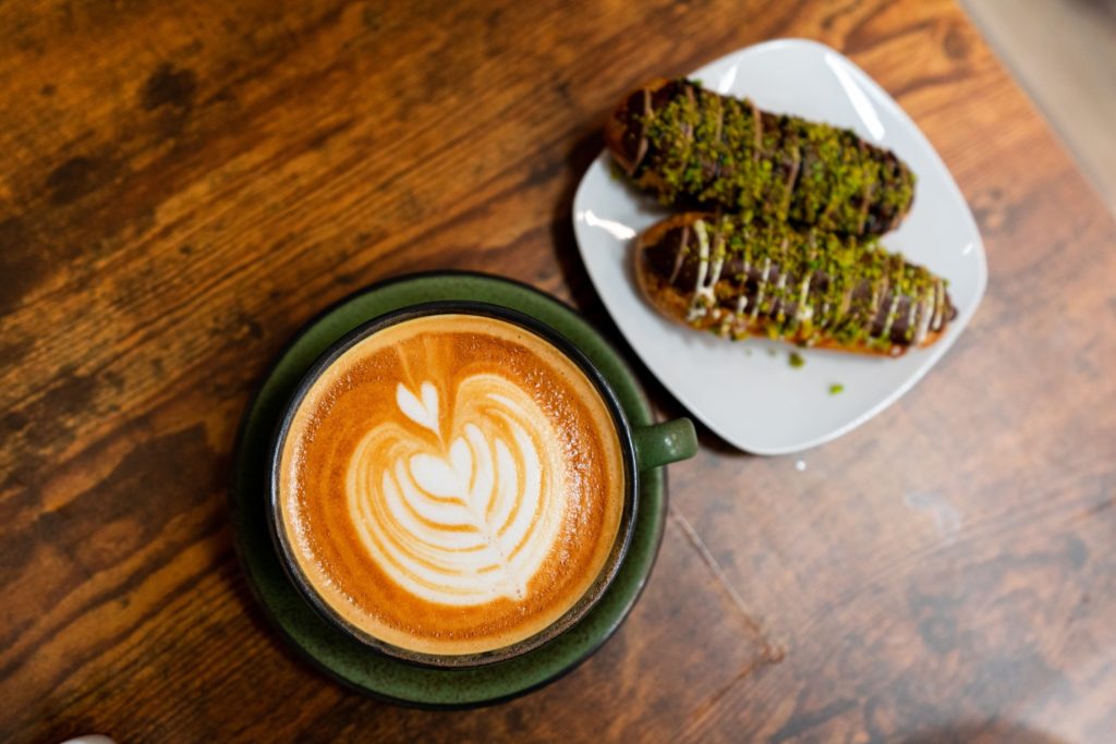 close up of latte and crushed pistachio covered chocolate eclairs at My Cravingz's 