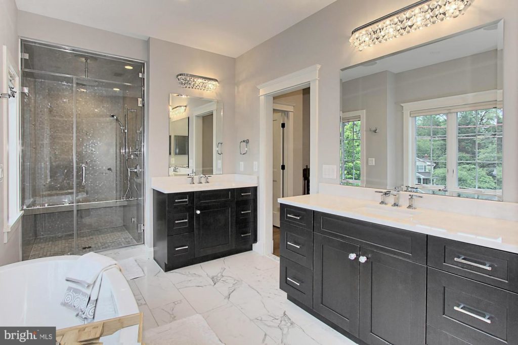 luxury contemporary bathroom with marble flooring, black cabinetry, white countertops, sleek stainless accents, a separate shower and soaking tub, and tons of natural lighting. 