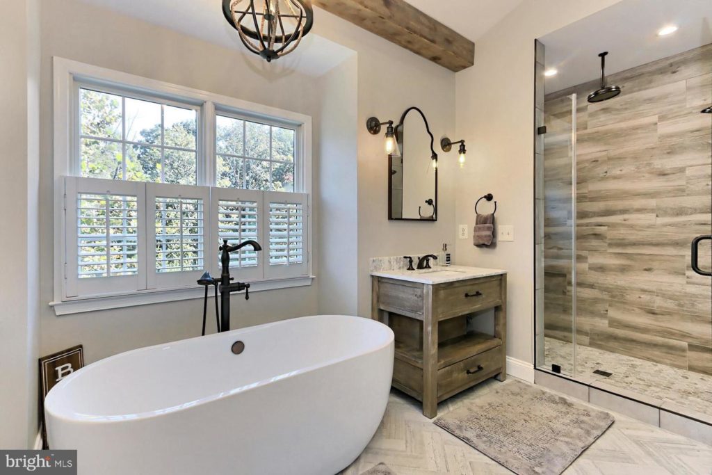 rustic-style luxury bathroom with a wooden ceiling beam, separate shower and soaking tub, and separate his and hers vanities